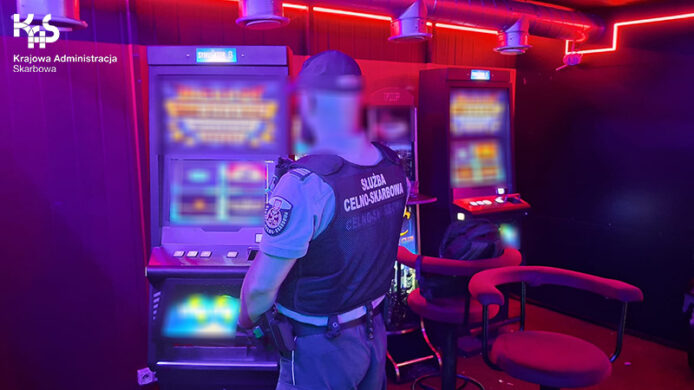 Funkcjonariusz Służby Celno-Skarbowej stoi przed automatem do gier. Twarz funkcjonariusza jest zanonimizowana.